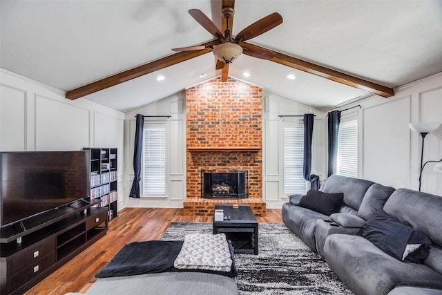 living room featuring vaulted ceiling with beams, ceiling fan, a fireplace, and hardwood / wood-style flooring