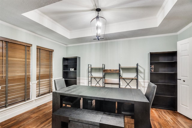 dining area featuring a raised ceiling, wood-type flooring, and ornamental molding