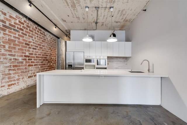 kitchen with stainless steel built in refrigerator, pendant lighting, white cabinets, and brick wall