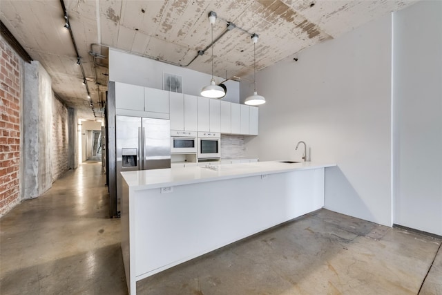 kitchen with sink, white oven, built in refrigerator, pendant lighting, and white cabinets