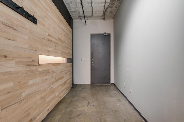 hall featuring wood walls and concrete floors