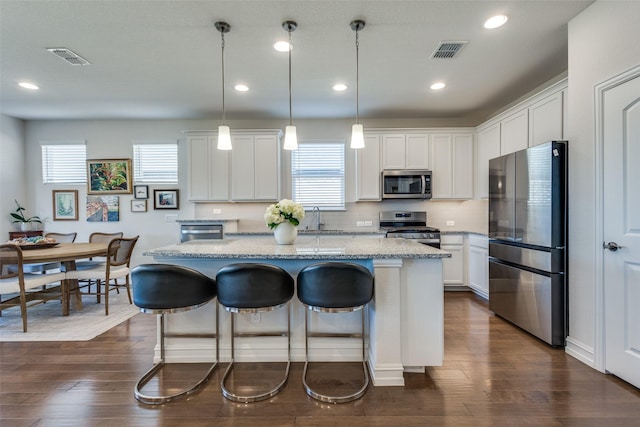 kitchen with light stone counters, stainless steel appliances, white cabinets, a center island, and hanging light fixtures