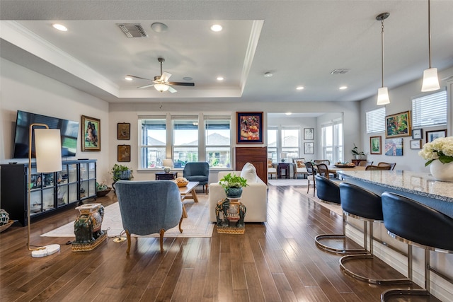 living room featuring hardwood / wood-style flooring, ceiling fan, a raised ceiling, and ornamental molding