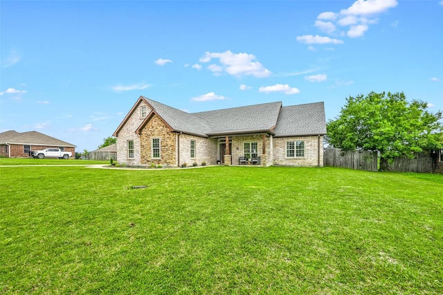 view of front of home with stone siding, a shingled roof, a front lawn, and fence