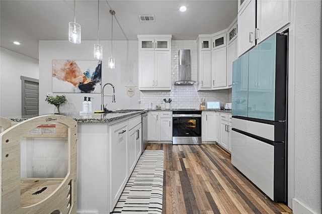 kitchen featuring wall chimney exhaust hood, white cabinetry, stainless steel appliances, and dark stone counters