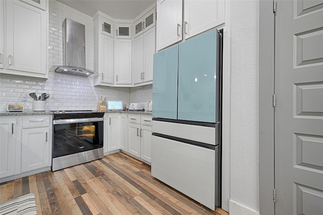 kitchen featuring wall chimney exhaust hood, refrigerator, stainless steel range oven, and white cabinetry