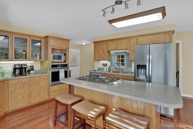 kitchen with a kitchen breakfast bar, sink, stainless steel appliances, and light hardwood / wood-style floors