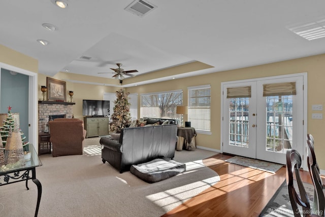 living room featuring french doors, a tray ceiling, ceiling fan, a fireplace, and light hardwood / wood-style floors