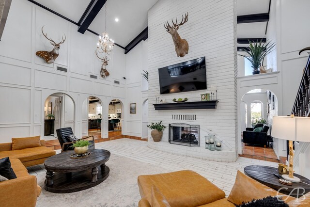 living room featuring a brick fireplace, a towering ceiling, a chandelier, and beam ceiling