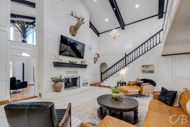 living room featuring beam ceiling, a brick fireplace, a towering ceiling, and a chandelier