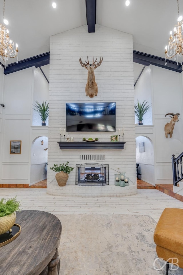 living room with an inviting chandelier, a brick fireplace, and lofted ceiling with beams