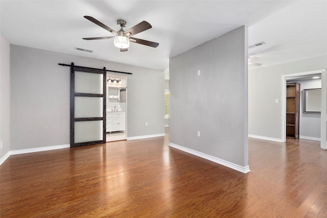 empty room with ceiling fan, a barn door, and wood-type flooring