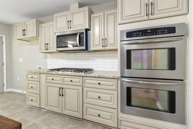 kitchen with cream cabinetry, decorative backsplash, light stone countertops, and appliances with stainless steel finishes