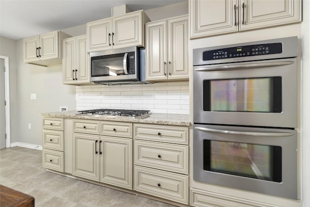 kitchen featuring stainless steel appliances, light stone countertops, backsplash, and cream cabinetry