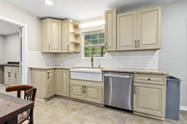 kitchen with light stone counters, stainless steel dishwasher, sink, and cream cabinetry