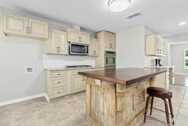 kitchen featuring butcher block counters, a breakfast bar area, tasteful backsplash, stainless steel appliances, and cream cabinetry