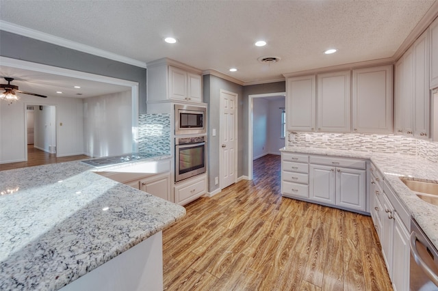 kitchen with ornamental molding, appliances with stainless steel finishes, light stone counters, and light hardwood / wood-style floors