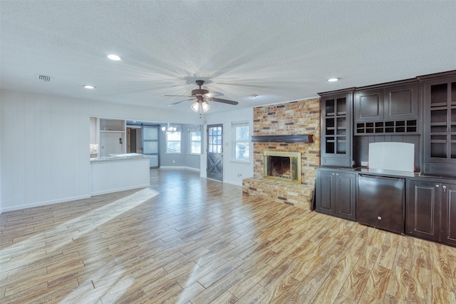 unfurnished living room featuring ceiling fan, a fireplace, a textured ceiling, and light wood-type flooring