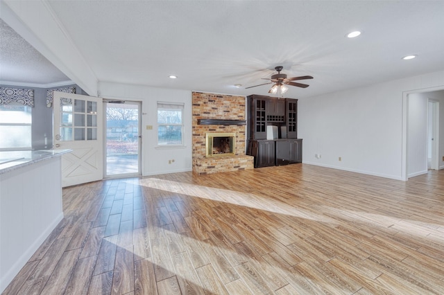 unfurnished living room with ceiling fan, crown molding, and a brick fireplace