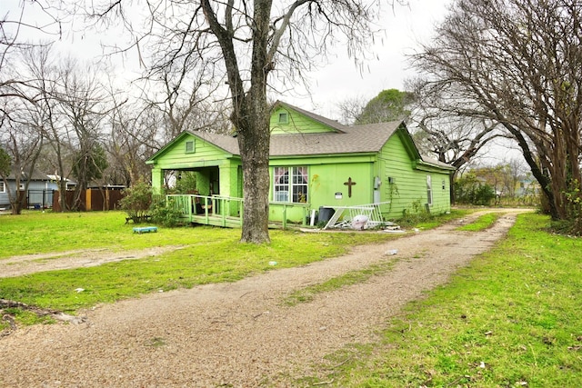 rear view of property featuring driveway, roof with shingles, fence, and a yard