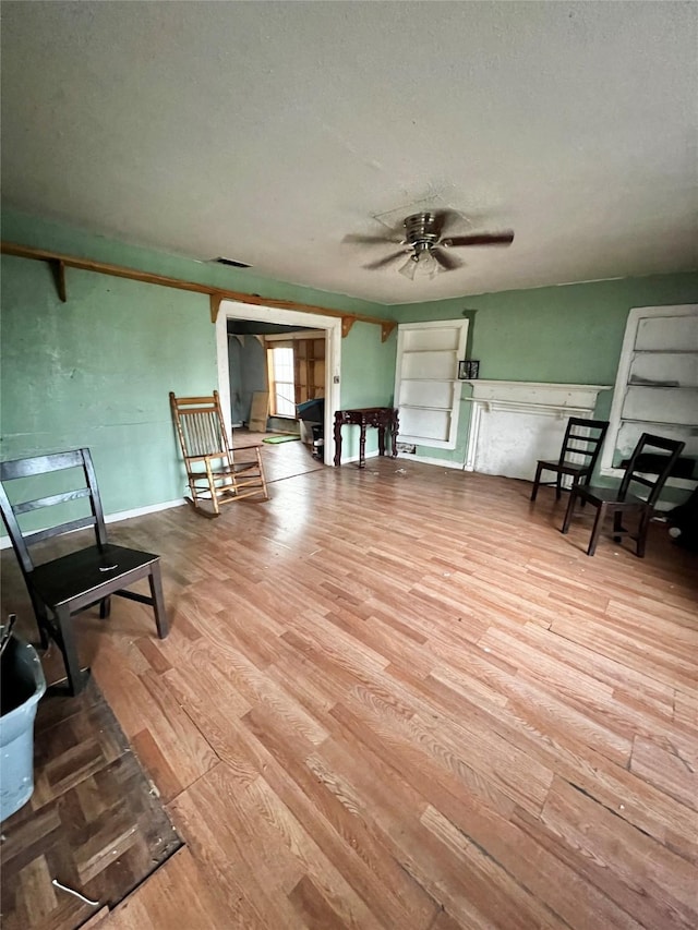 living area with ceiling fan, a textured ceiling, visible vents, and wood finished floors