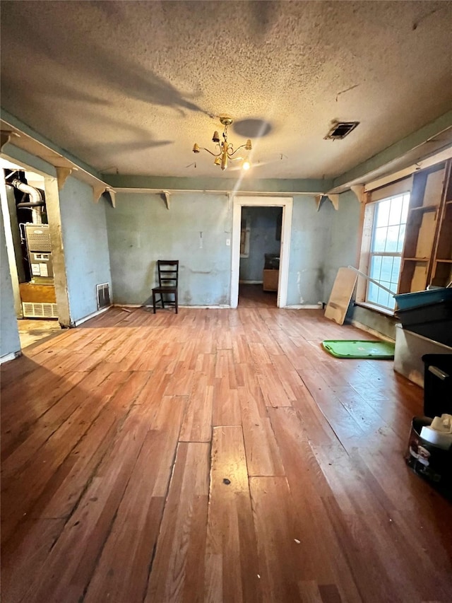 unfurnished living room with visible vents, a textured ceiling, hardwood / wood-style flooring, and an inviting chandelier