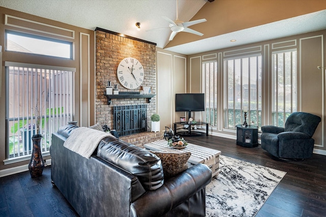 living room with vaulted ceiling, ceiling fan, a brick fireplace, dark wood-type flooring, and a textured ceiling