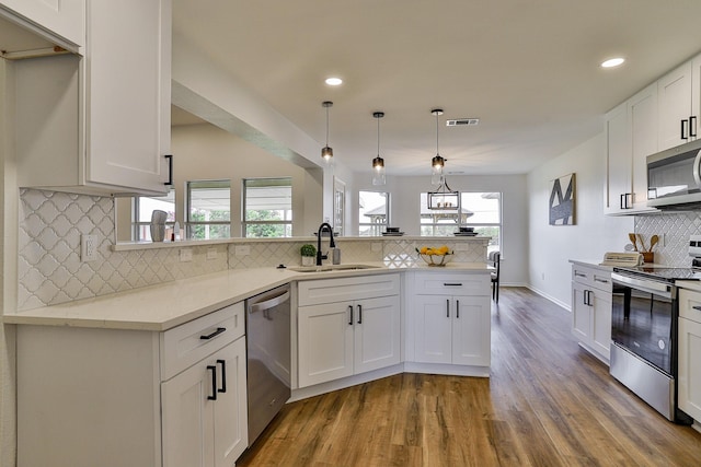 kitchen featuring pendant lighting, sink, white cabinetry, kitchen peninsula, and stainless steel appliances