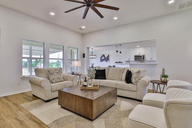 living room with ceiling fan with notable chandelier and light hardwood / wood-style flooring