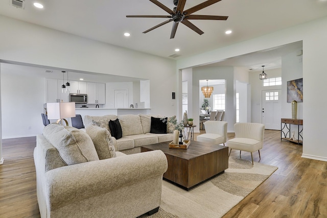 living room featuring ceiling fan with notable chandelier and light hardwood / wood-style floors