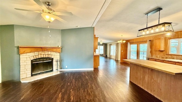 unfurnished living room featuring ceiling fan with notable chandelier, a fireplace, baseboards, and dark wood-style flooring