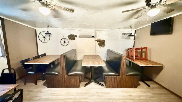 dining space with an AC wall unit, wood finished floors, baseboards, and ceiling fan