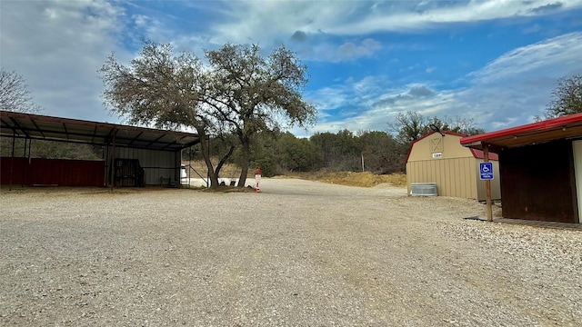 view of yard with gravel driveway, an outbuilding, cooling unit, and a carport