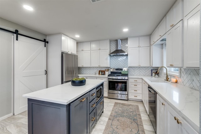 kitchen featuring white cabinetry, appliances with stainless steel finishes, a kitchen island, a barn door, and wall chimney range hood