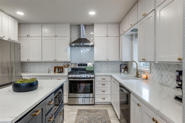 kitchen featuring wall chimney exhaust hood, sink, stainless steel appliances, light stone countertops, and white cabinets