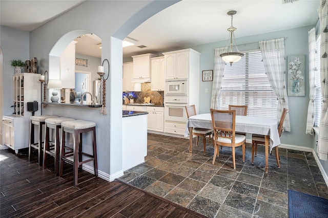 kitchen with white cabinetry, backsplash, kitchen peninsula, decorative light fixtures, and white appliances