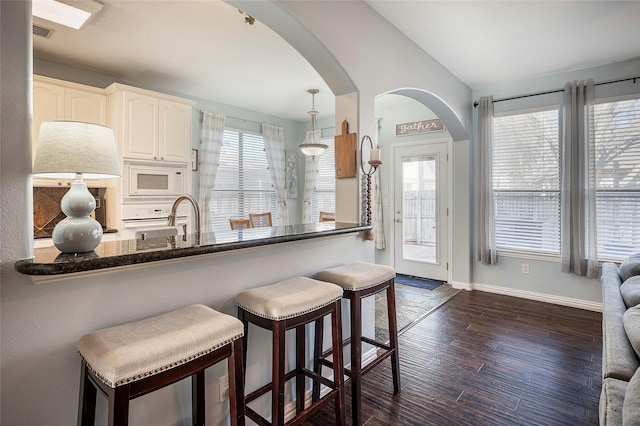 kitchen with white cabinetry, a healthy amount of sunlight, dark hardwood / wood-style flooring, kitchen peninsula, and white microwave