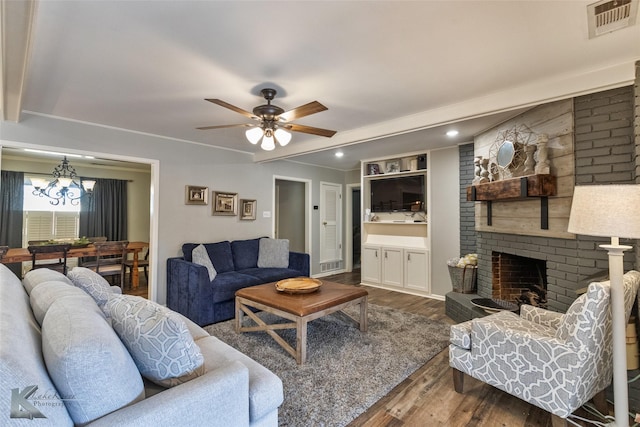 living room featuring crown molding, a brick fireplace, hardwood / wood-style flooring, built in features, and ceiling fan with notable chandelier