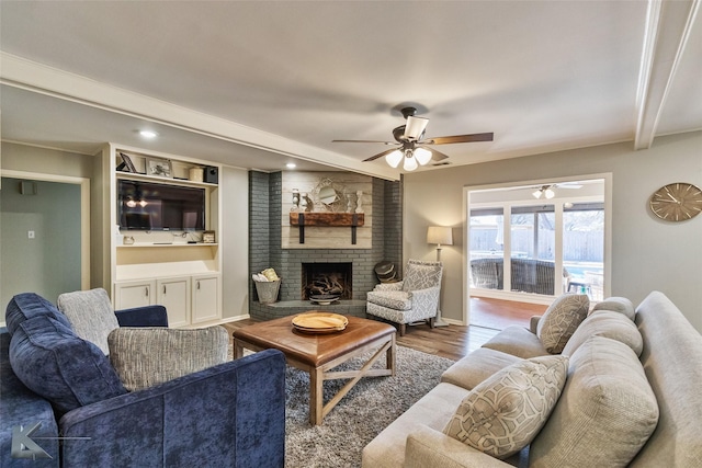 living room featuring beamed ceiling, a fireplace, ceiling fan, and wood-type flooring