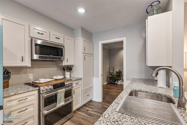 kitchen featuring white cabinets, stainless steel appliances, light stone countertops, dark wood-type flooring, and sink