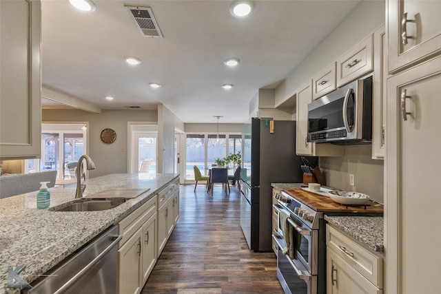 kitchen featuring light stone counters, a healthy amount of sunlight, hanging light fixtures, stainless steel appliances, and sink