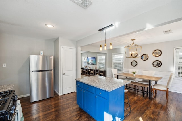 kitchen with appliances with stainless steel finishes, blue cabinets, hanging light fixtures, a center island, and light stone countertops