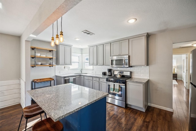 kitchen featuring sink, hanging light fixtures, gray cabinets, stainless steel appliances, and light stone countertops