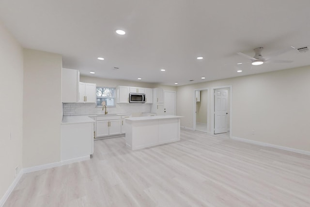 kitchen with ceiling fan, a center island, backsplash, white cabinets, and light wood-type flooring