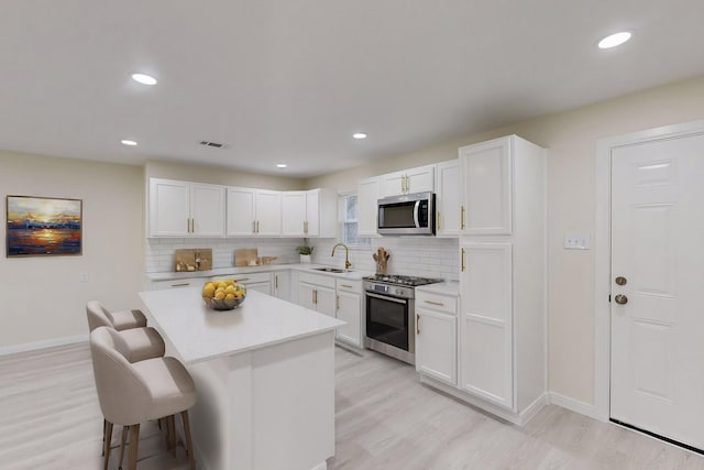 kitchen featuring appliances with stainless steel finishes, tasteful backsplash, a kitchen island, white cabinetry, and a breakfast bar area