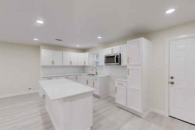 kitchen featuring white cabinets, a kitchen island, light hardwood / wood-style floors, and backsplash