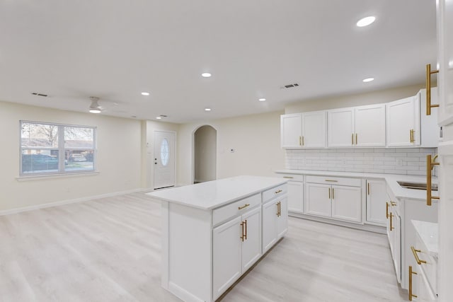 kitchen featuring light wood-type flooring, backsplash, a kitchen island, ceiling fan, and white cabinetry