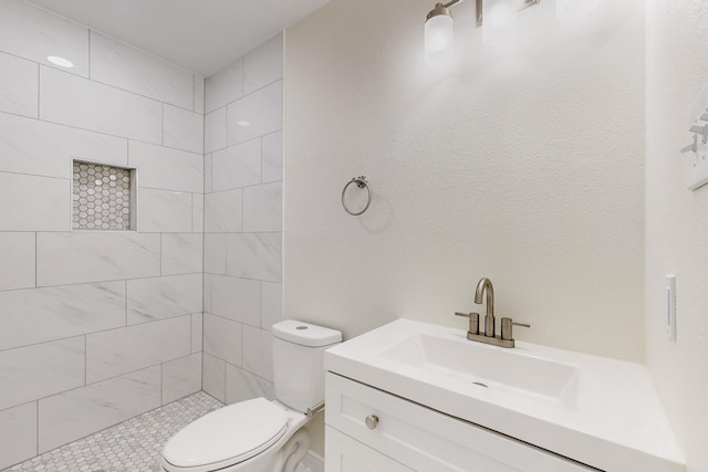 bathroom with tiled shower, vanity, and toilet