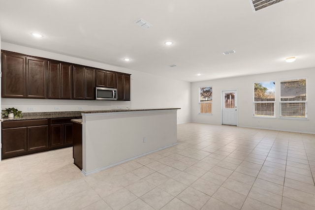 kitchen with dark brown cabinetry, an island with sink, and light tile patterned floors