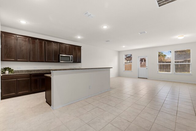 kitchen with dark brown cabinets, a kitchen island with sink, and light tile patterned floors